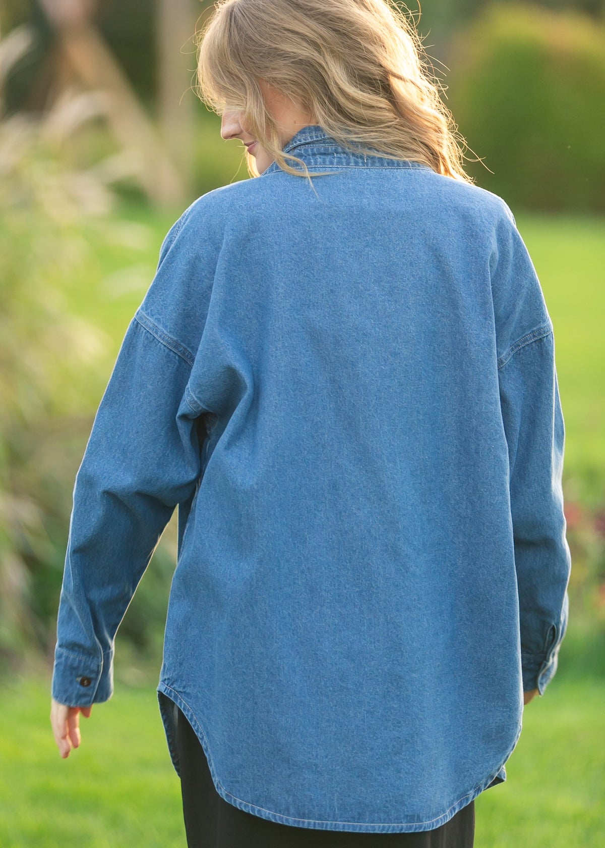 Denim button-up top in medium blue, back view with long sleeves and curved hem.