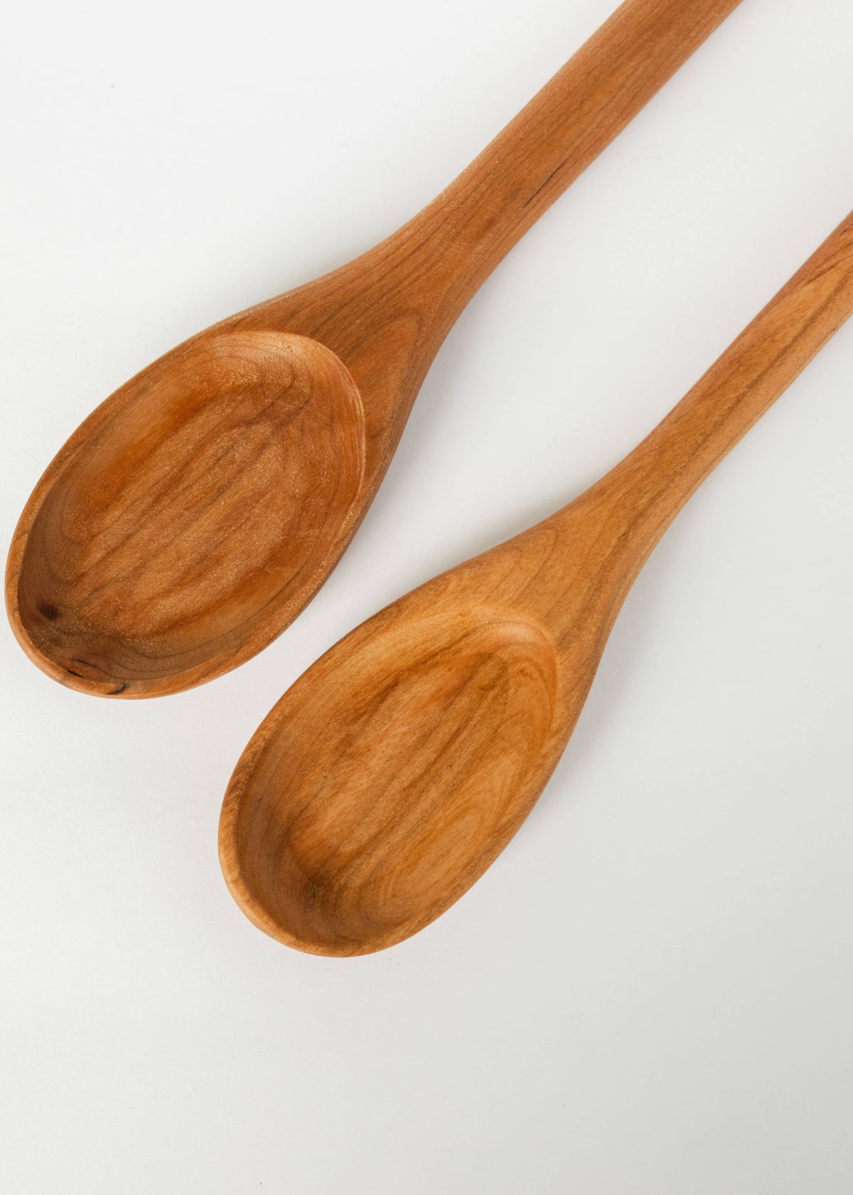 Two orange-brown wooden spoons, oval bowls with smooth finish and long handles.