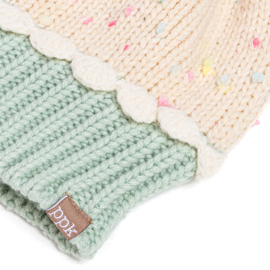 Close-up of mint ribbed knit mitten with cream cuff and DKNY-style leather brand tag.
