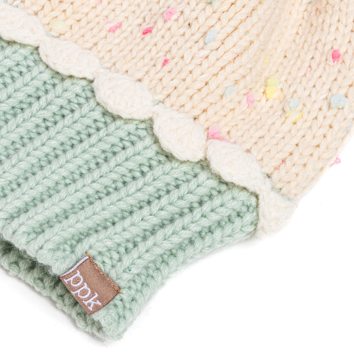Close-up of mint ribbed knit mitten with cream cuff and DKNY-style leather brand tag.
