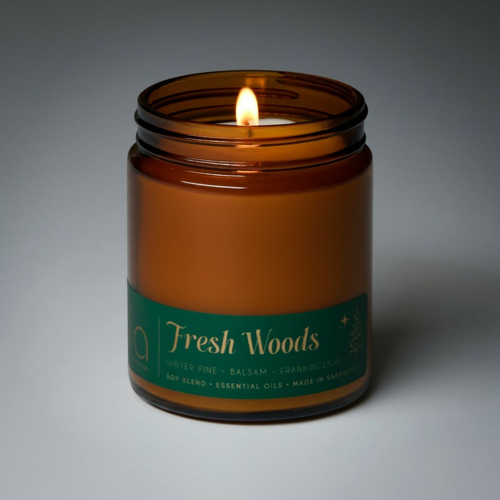 Amber soy candle in clear glass jar with lit wick and Fresh Woods label