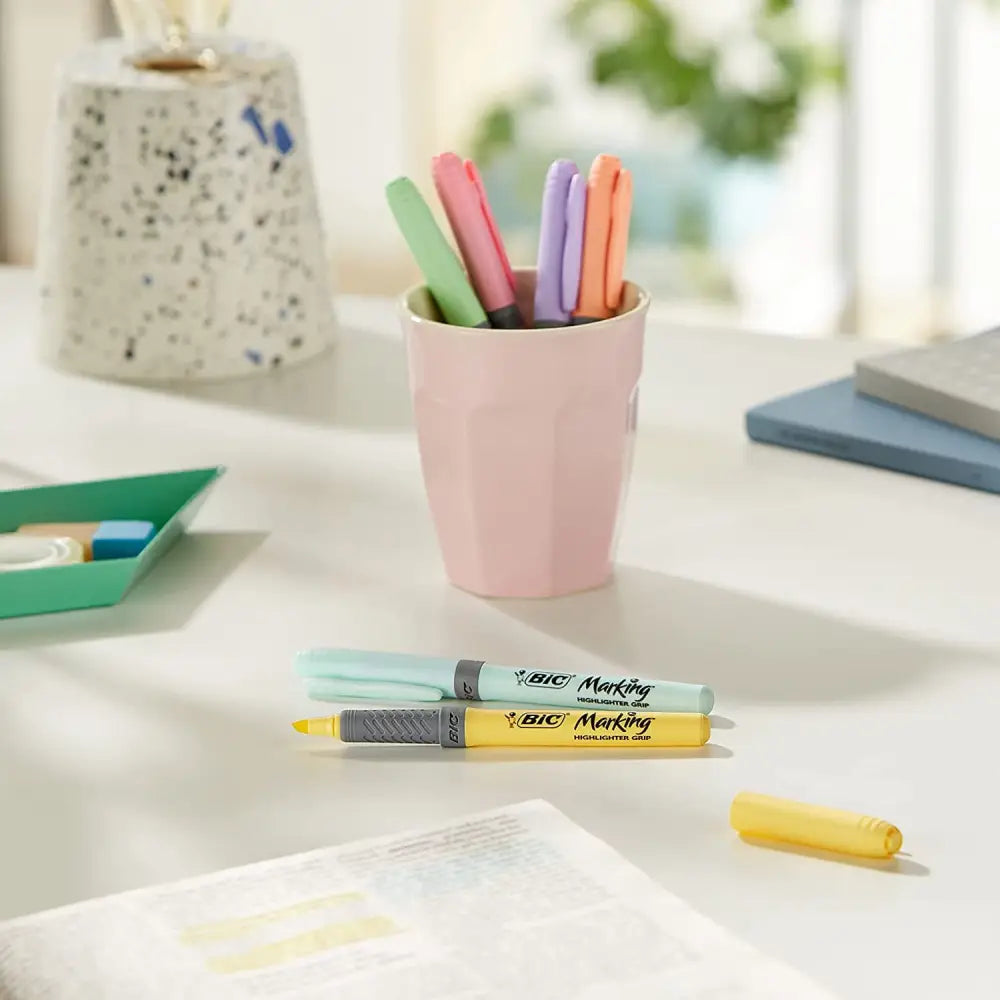 Pastel highlighter pens in a pink cup on a desk