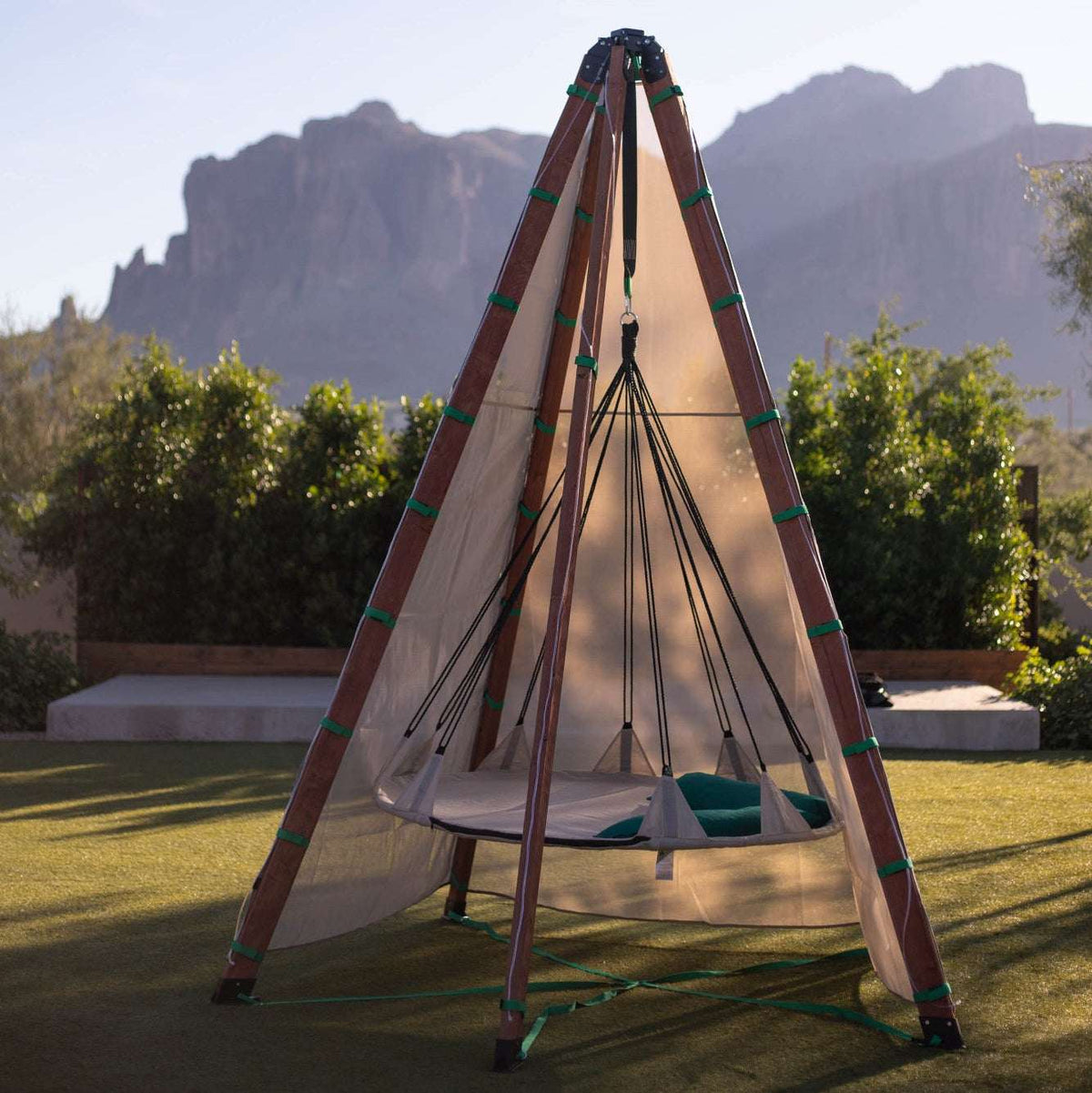 Triangular-frame hammock nest with net canopy, brown poles, and green base cushion