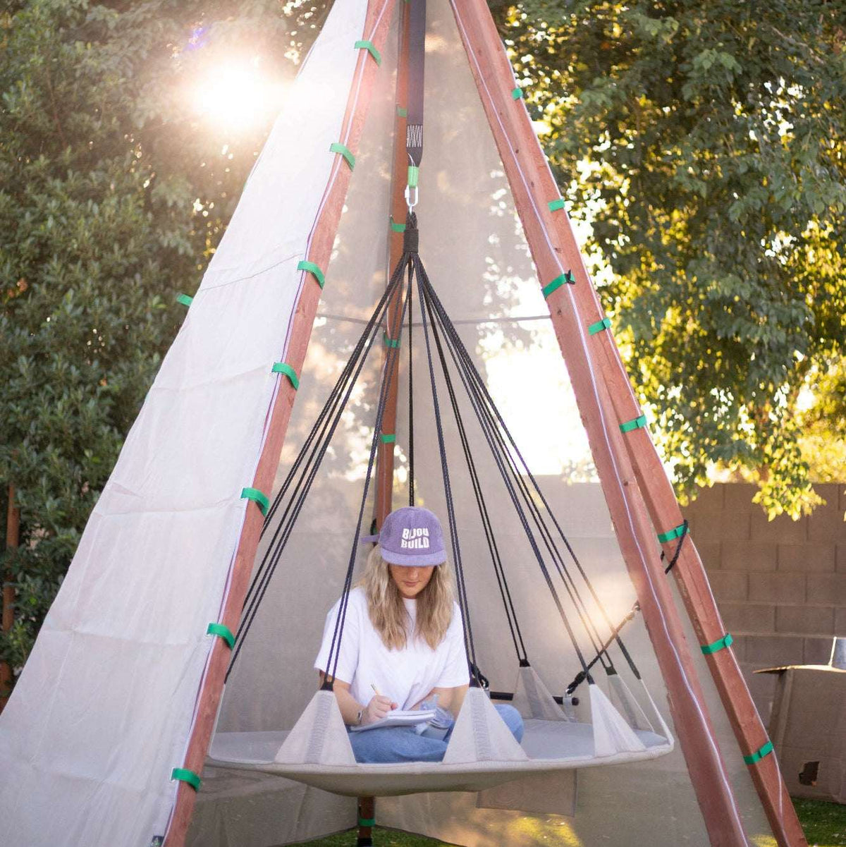 Off-white tipi play tent with wooden poles and black rope netting; person inside