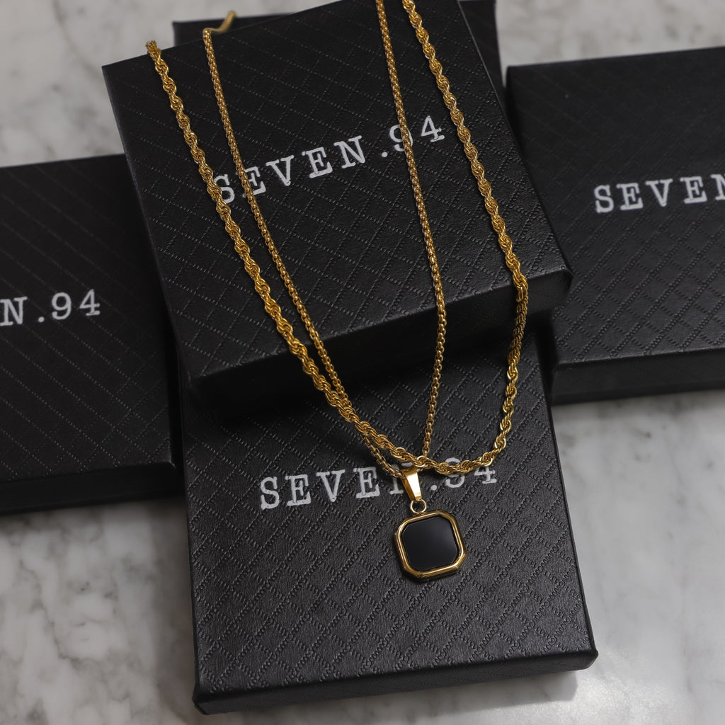 Gold-tone pendant necklace set with square black onyx charm laid on gift boxes