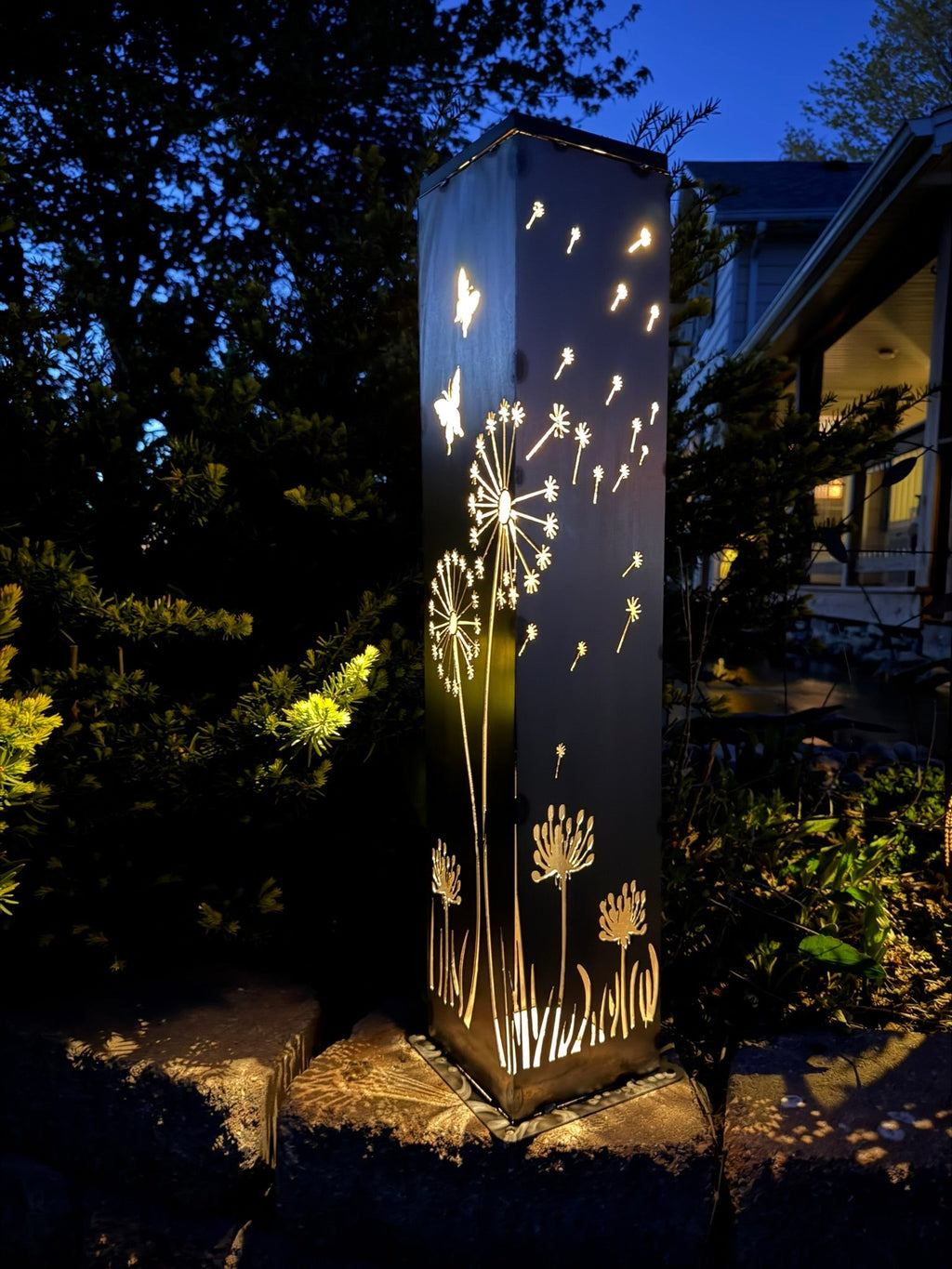 Solar steel luminary pillar light glowing with dandelion bursts and butterfly shapes