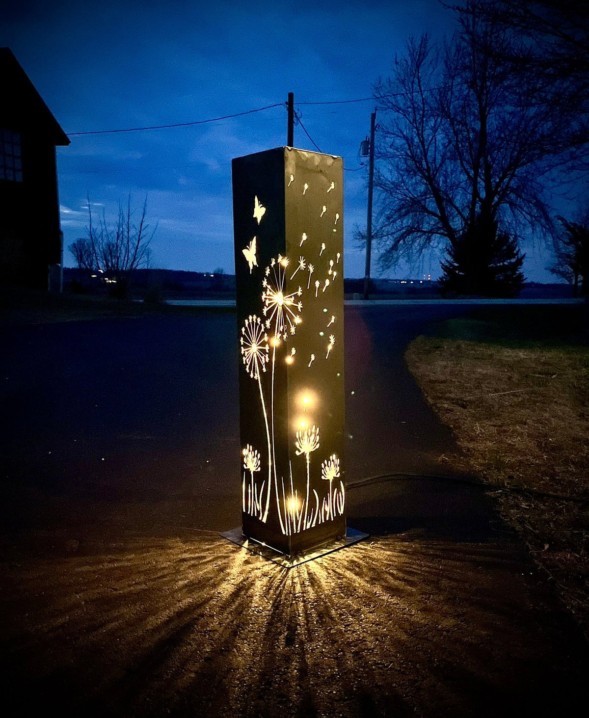 Solar steel luminary pillar light glowing through dandelion and butterfly silhouettes