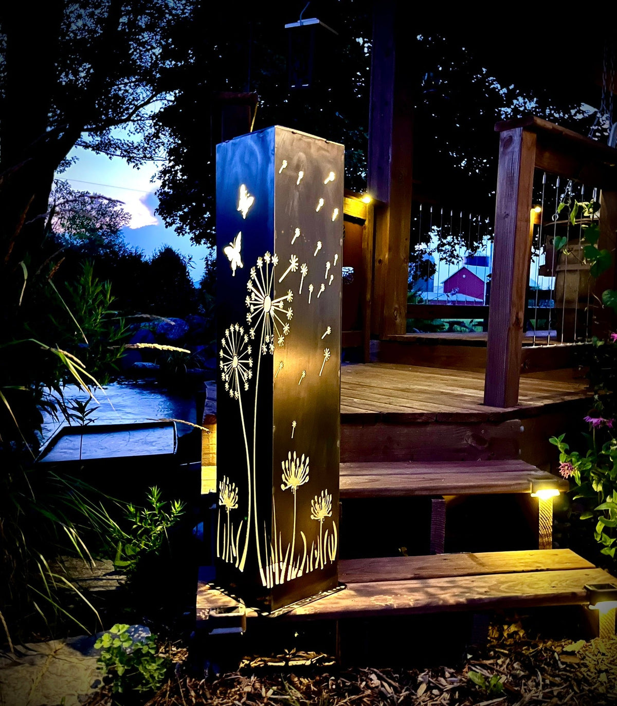 Solar steel luminary pillar light casting warm glow with dandelion and butterfly designs