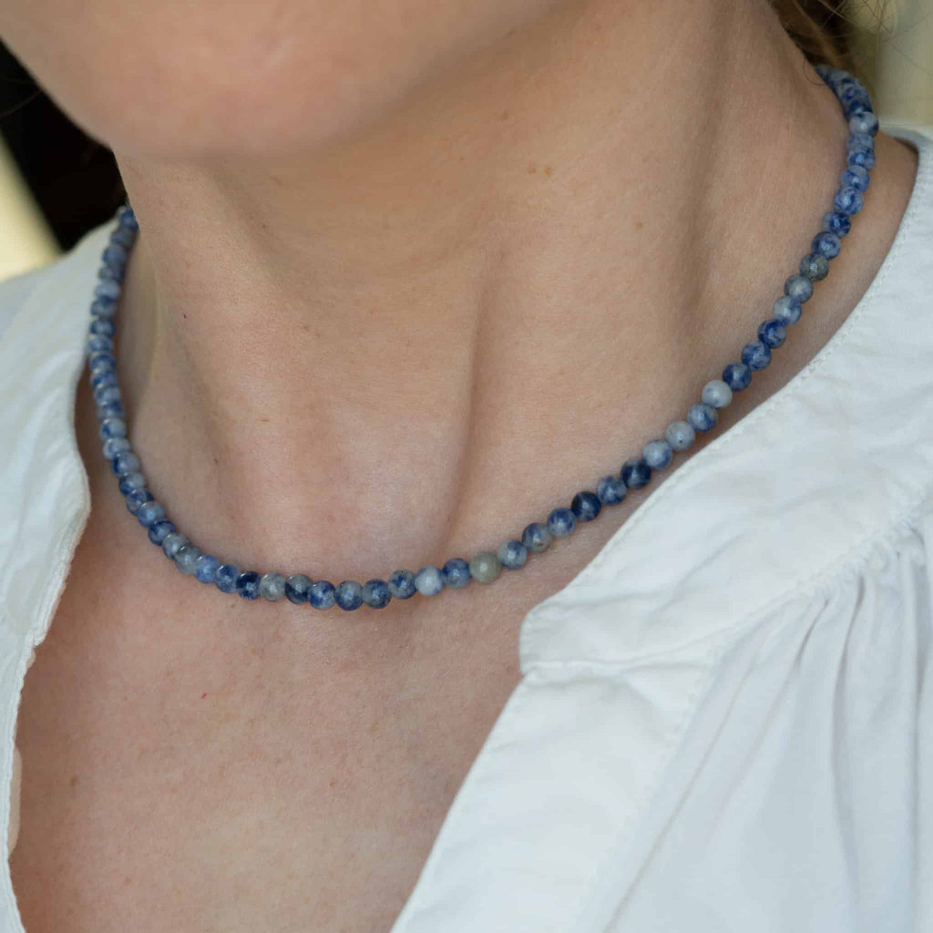 Blue beaded necklace with navy and light-blue round beads along the collarbone