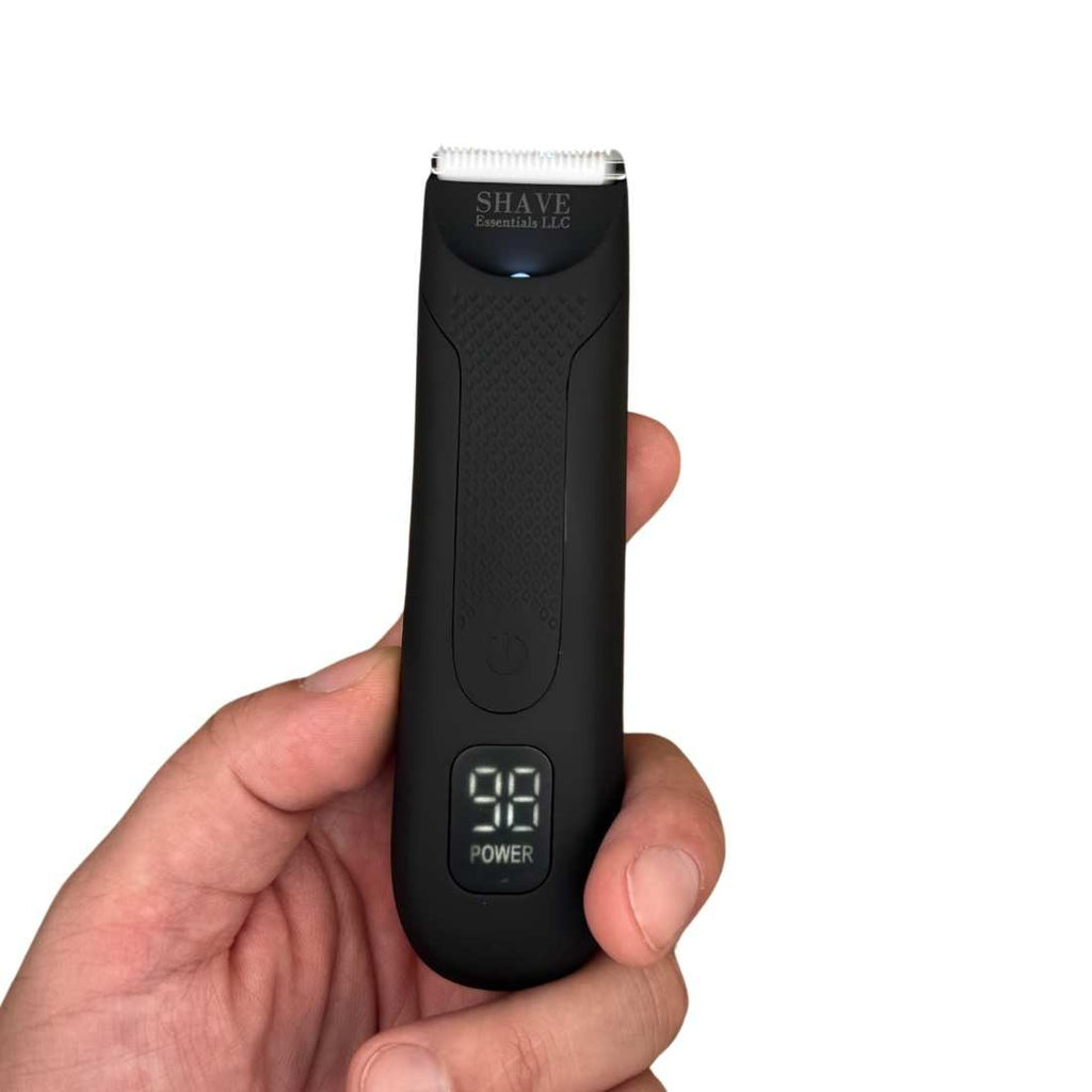 Black electric grooming shaver held in hand, with power button and display