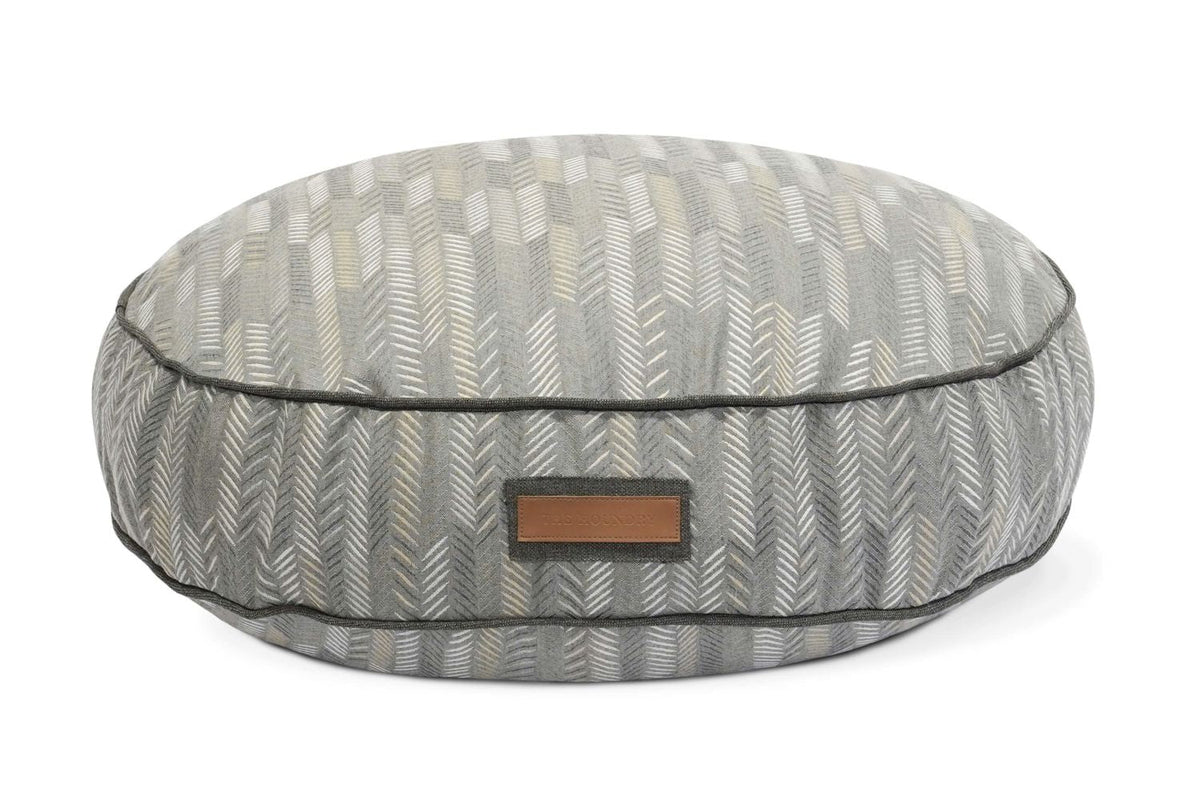 Round pet bed with gray chevron patterned fabric and a rectangular patch label