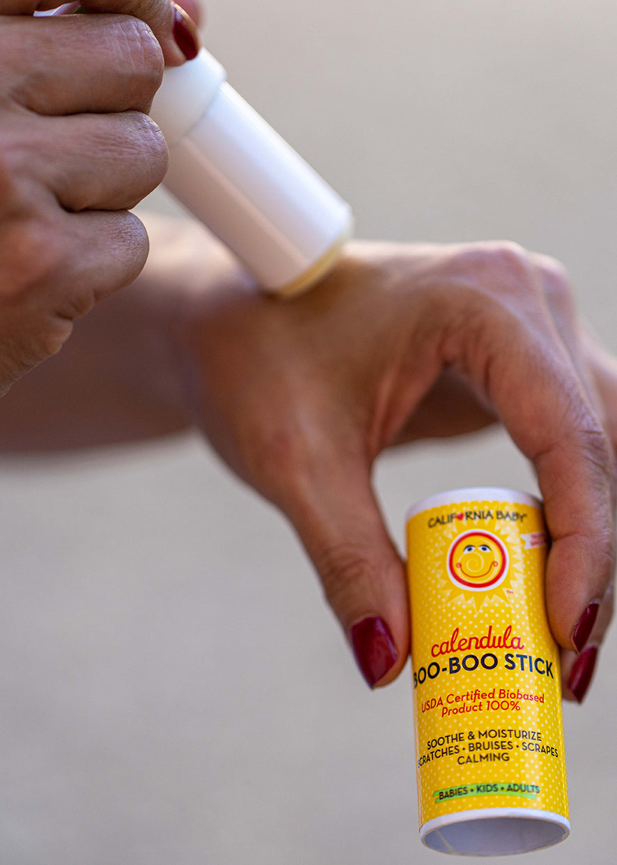 Hands applying Boo-Boo stick to skin, yellow tube held against leg