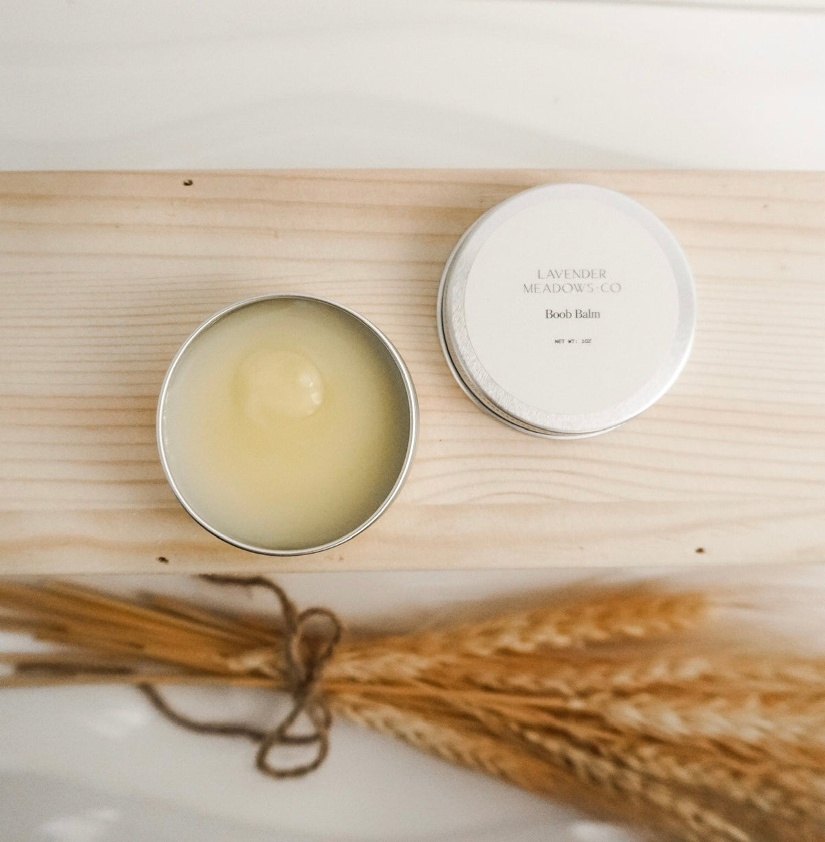Lavender Meadows Co body tin beside shallow jar with pale cream and bundled dried herbs