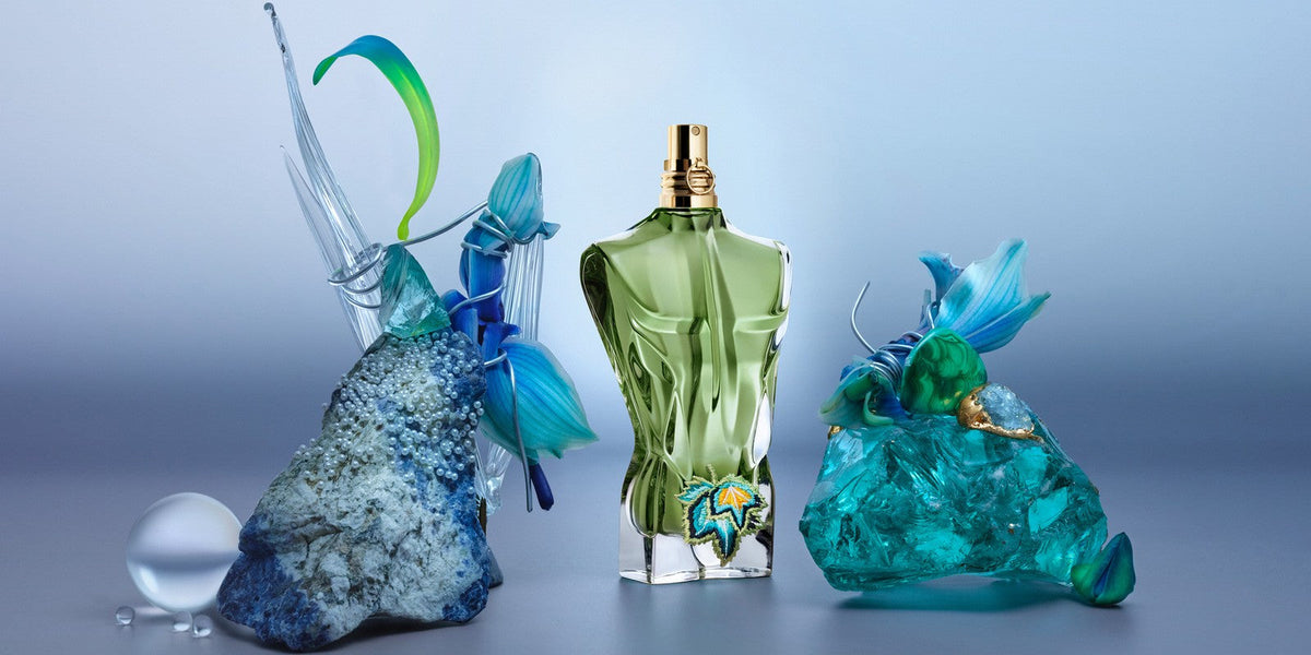 Green glass eau de parfum bottle with gold cap and starburst emblem amid blue decor