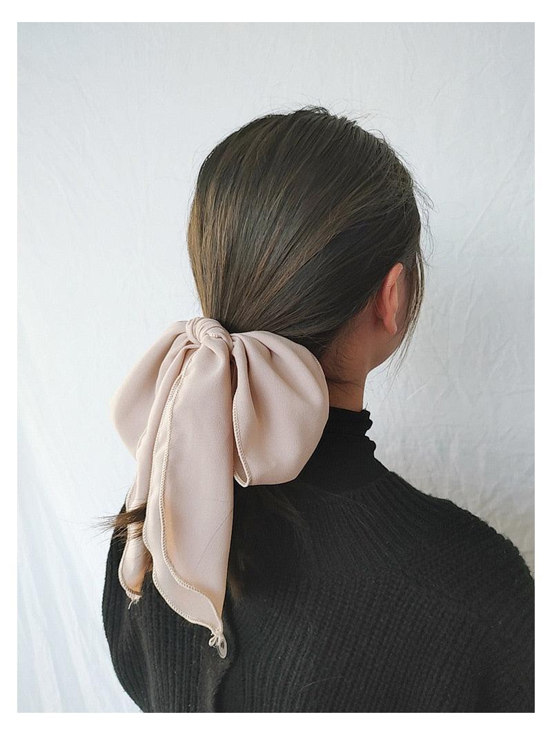 Beige bowknot hair scrunchie with long fabric tails on dark hair