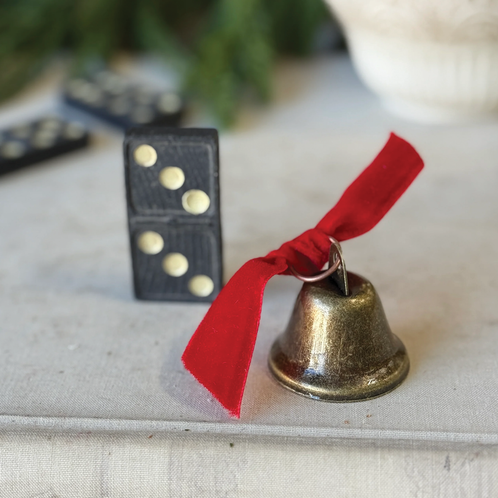 Decorative brass-tone bell ornament with red ribbon on white fabric.