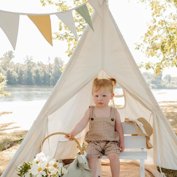 White kids teepee tent with floor mat outdoors, baby sitting inside by the window