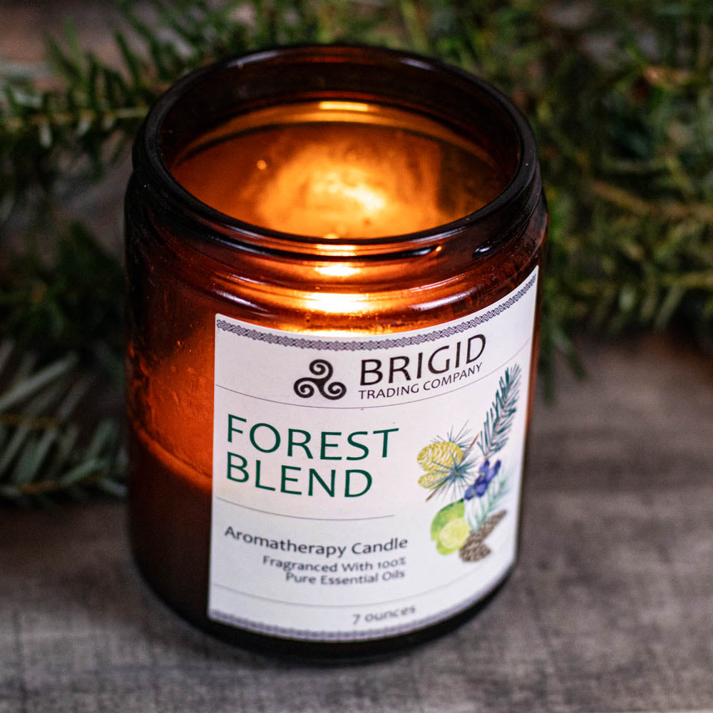 Amber glass soy wax candle with Forest Blend label, flame glowing inside the jar.