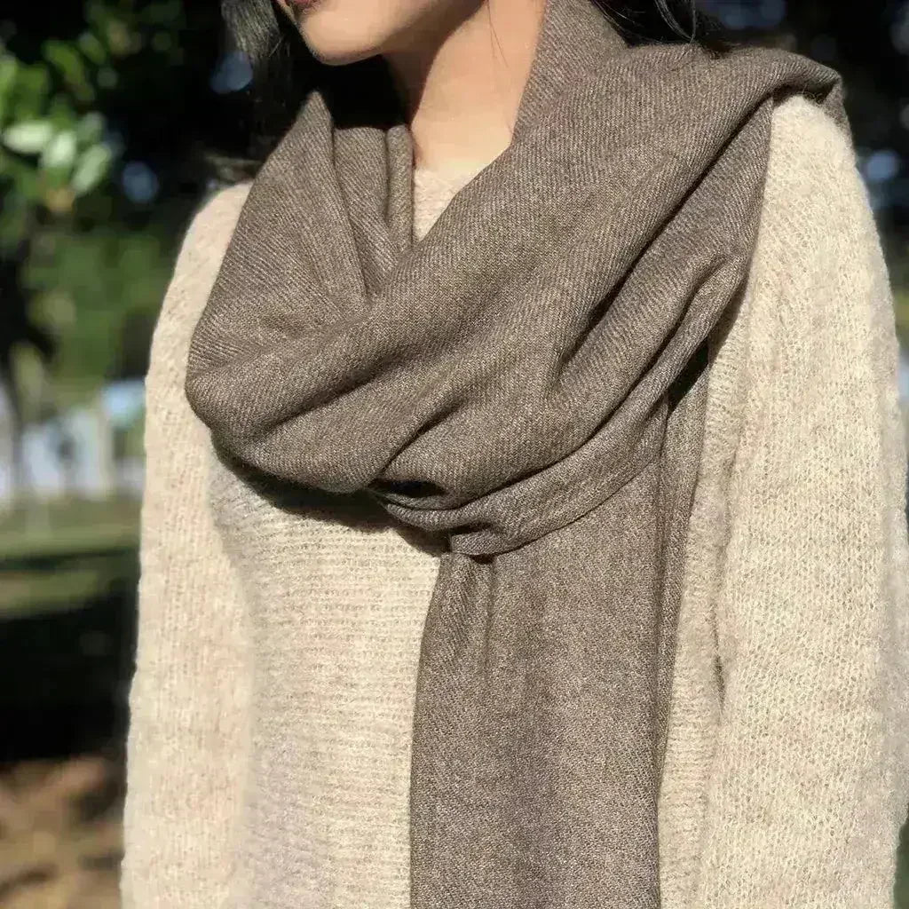 Draped cashmere scarf in taupe with fringed hem, wrapped around shoulders