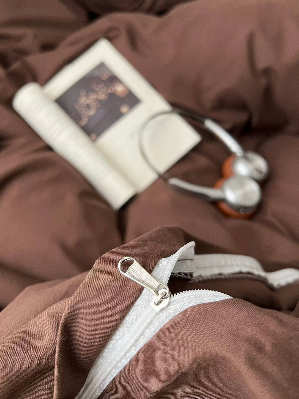 Dark brown bedding close-up: white zipper, fabric texture, and patterned tag detail