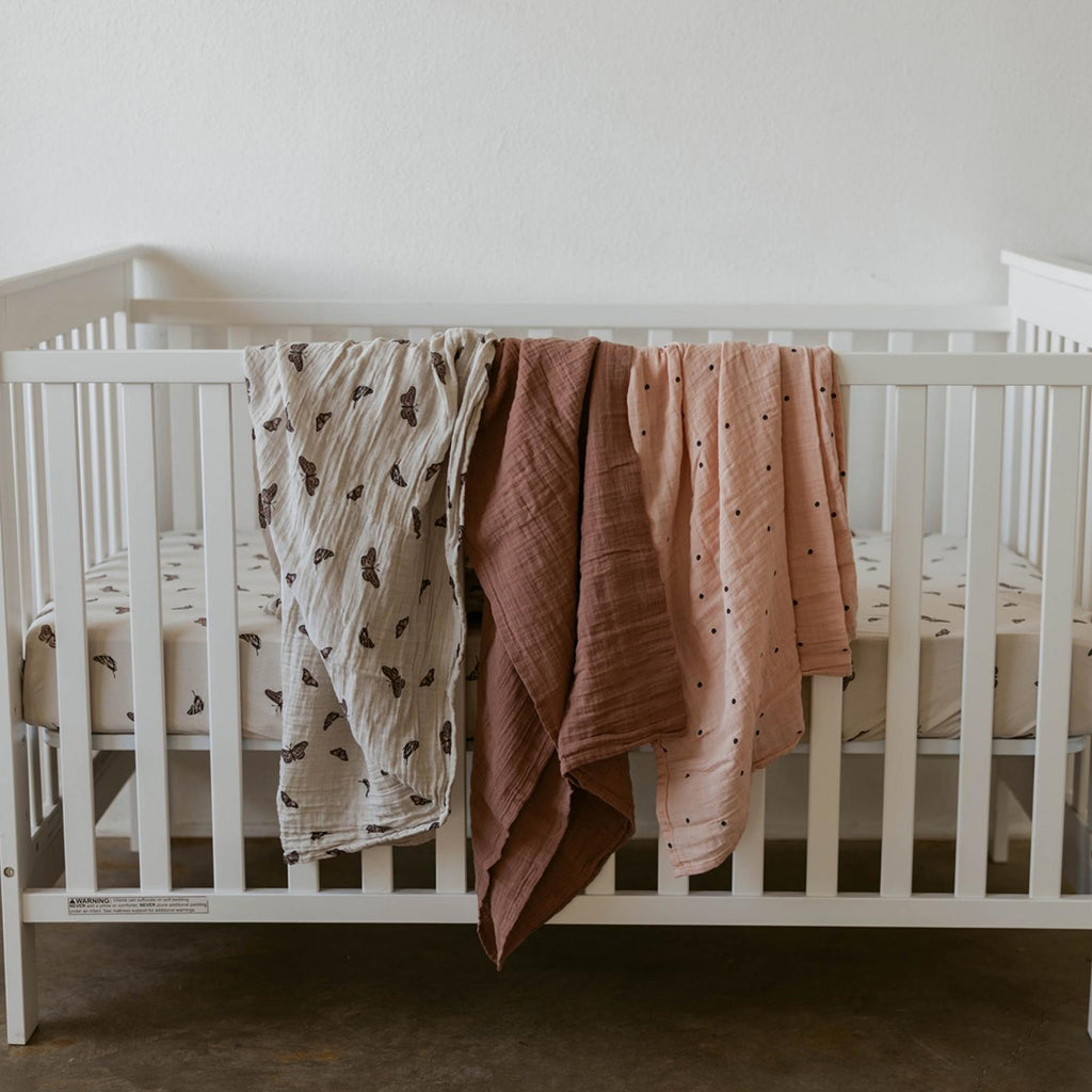 Butterfly swaddle set blankets draped over a white crib rail