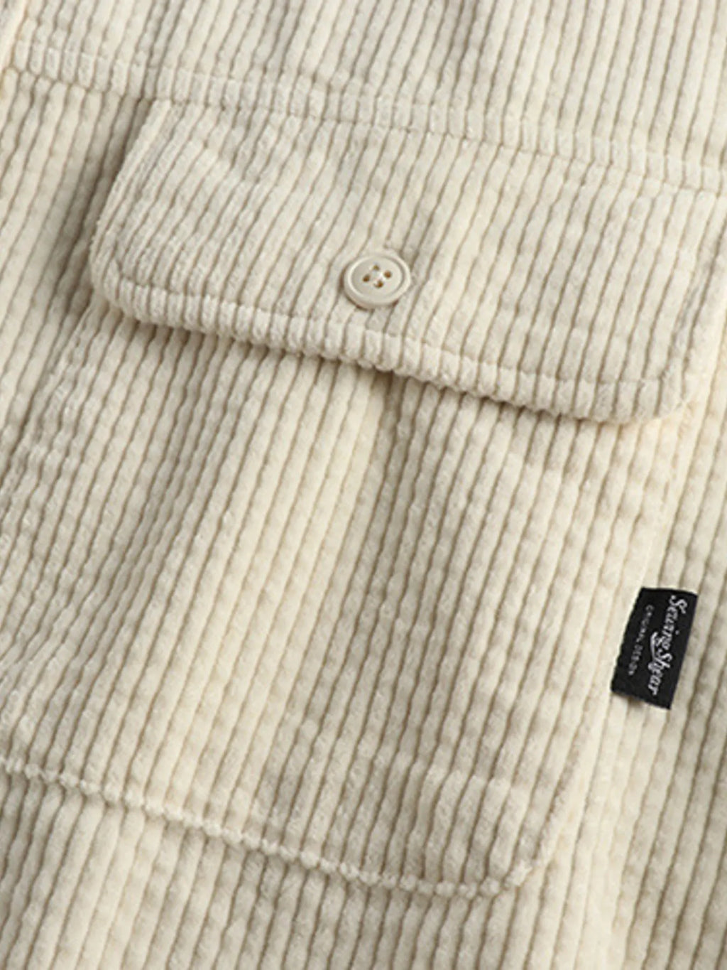 Close-up of light beige corduroy shirt hem with button and small side label