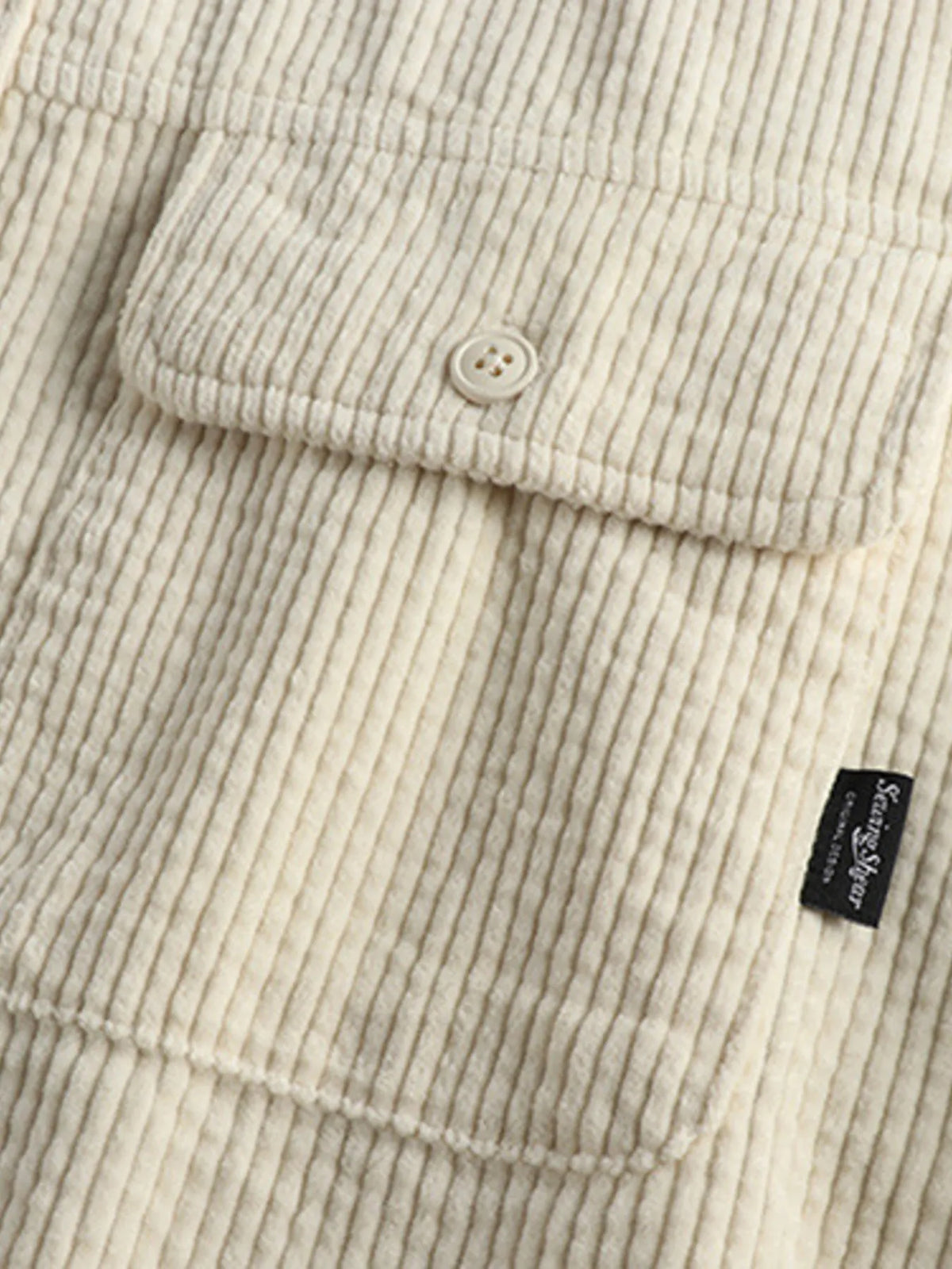 Close-up of light beige corduroy shirt hem with button and small side label
