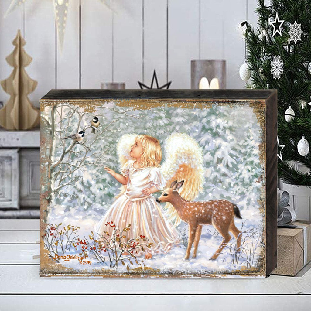 Framed wooden wall art with angel girl, deer, and snowy trees on a tabletop
