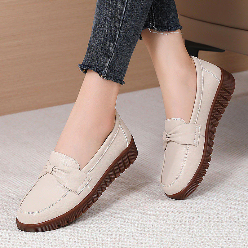 Women’s beige flat loafers with bow detail and ridged rubber sole under jeans