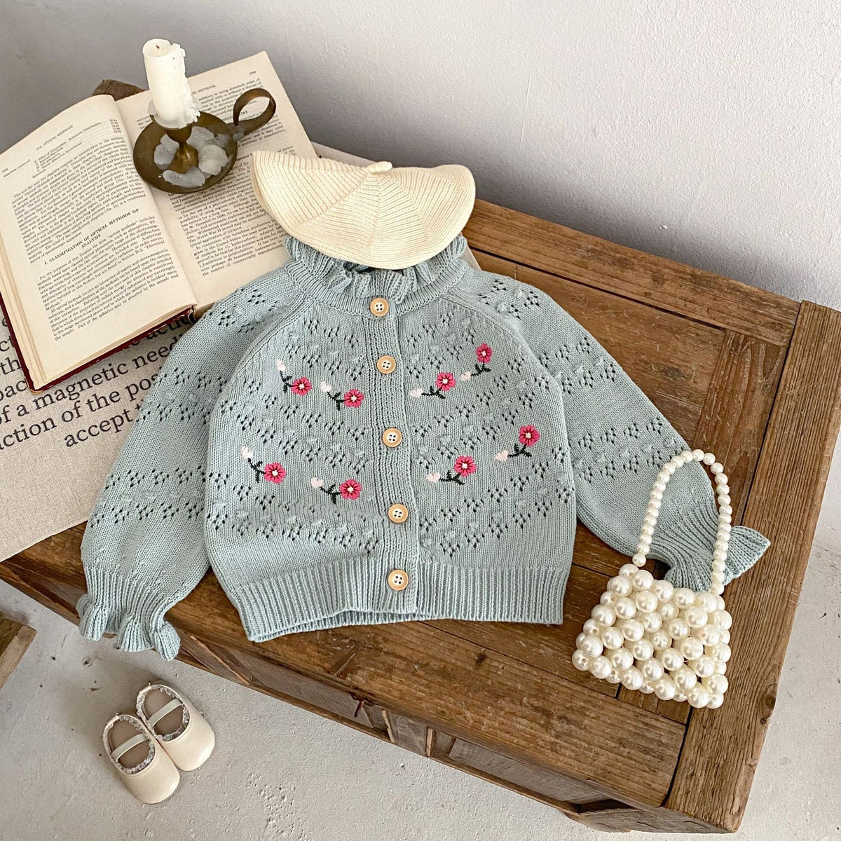 Blue-gray knitted cardigan with button front, ribbed cuffs, and red floral embroidery.