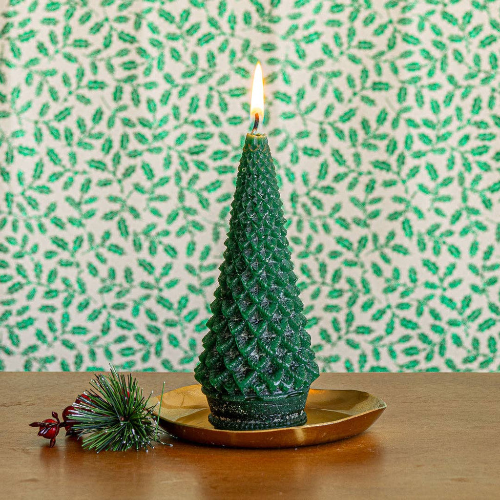 Green tree-shaped candle on round gold plate with pine brush and pinecone