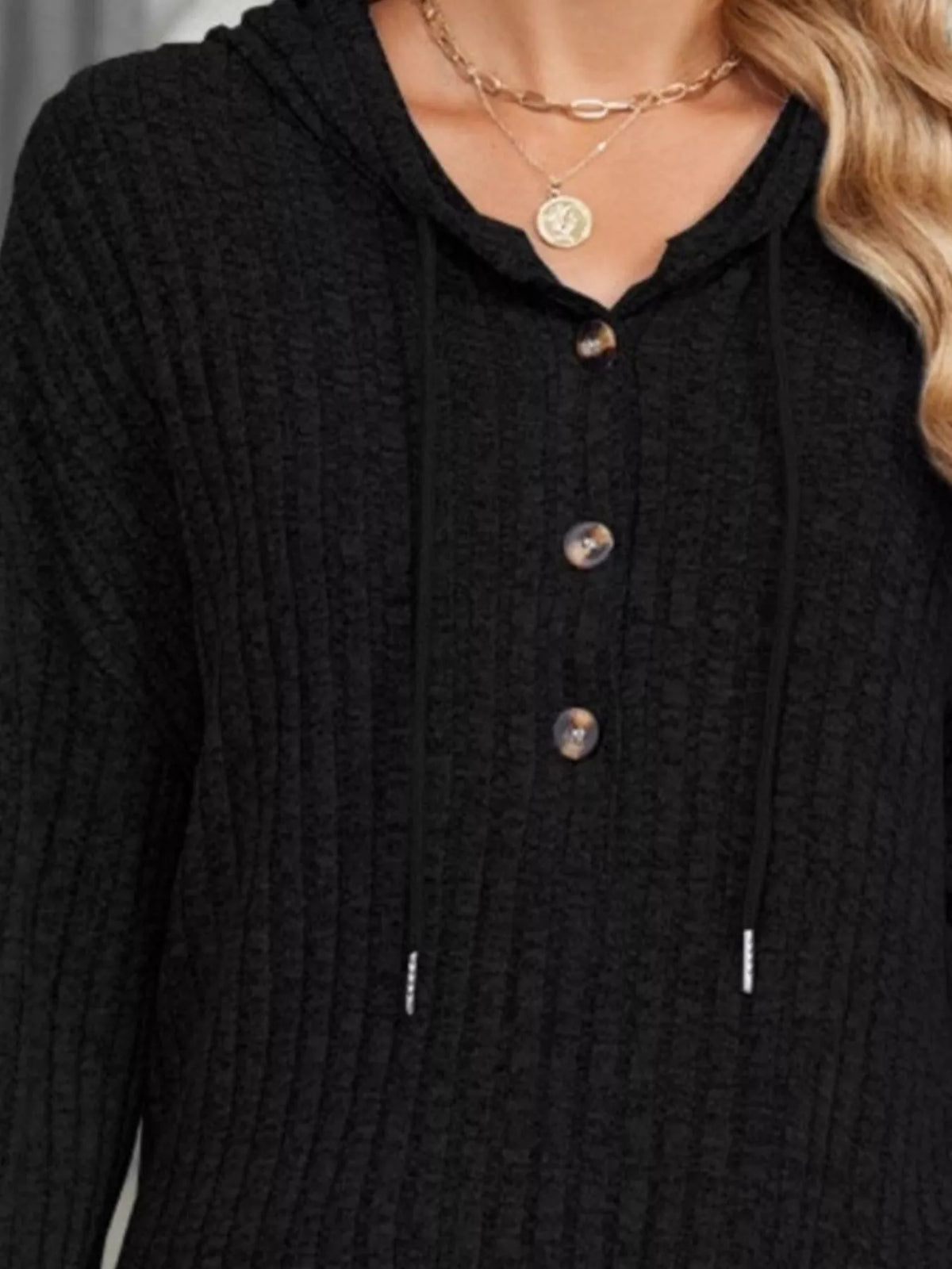 Black ribbed knit hoodie close-up: hood, button placket, and drawstring