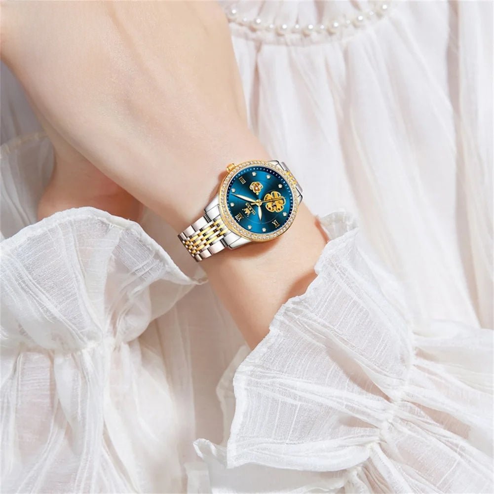 Two-tone automatic bracelet watch on wrist with blue floral dial and rhinestone bezel