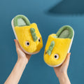 Kids’ yellow plush dragon slippers with green horns, held in hands