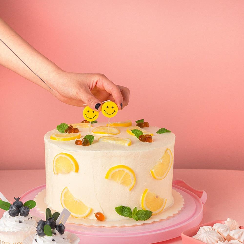 Hand placing smiley-faced candle toppers on a frosted birthday cake