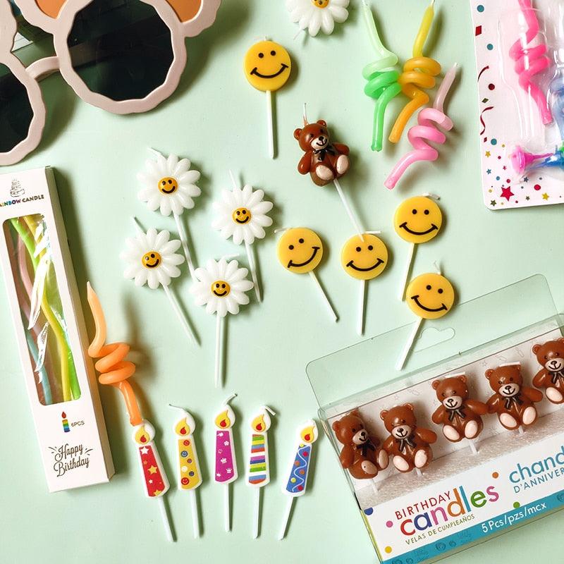 Cartoon birthday candle toppers with smiley faces and flower designs on sticks