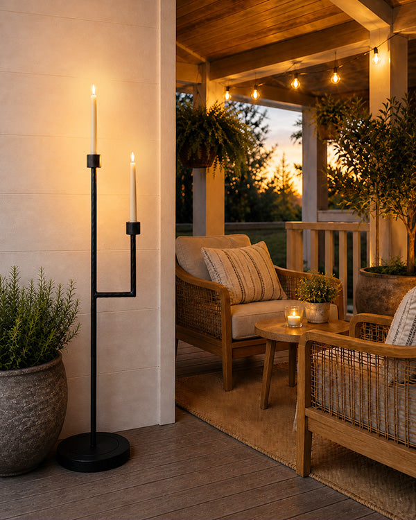 Black iron floor candelabra with two tall lit candles and square-to-round base.