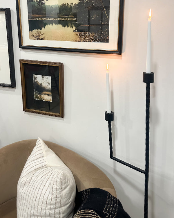 Black iron floor candelabra with two lit candle holders on metal stand.