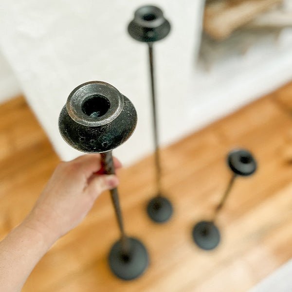 Close-up of a dark cast iron candle holder top and stem with a round candle cup.