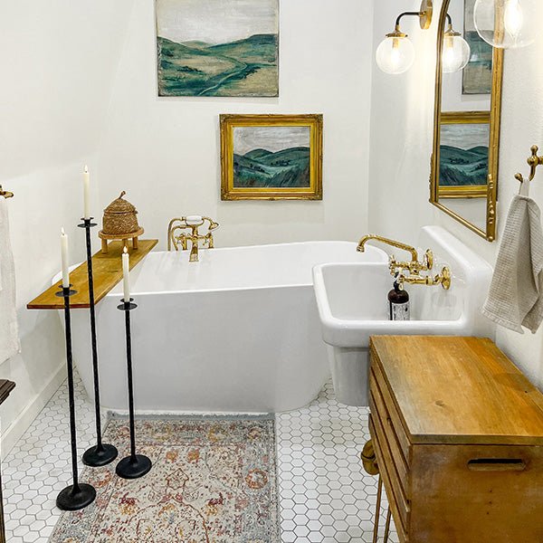 Three tall floor candle holders in black with round bases placed near a bathtub area.