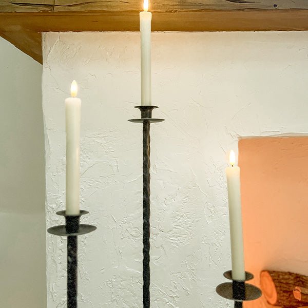 Close-up of tall dark cast iron candle holders with circular cups and candle sticks.