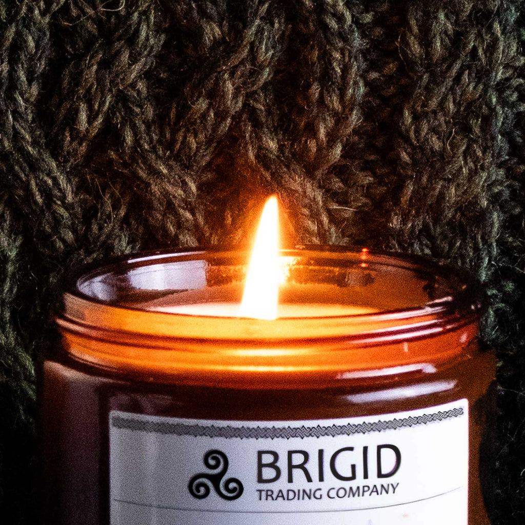Brigid scented soy candle burning in amber glass jar with bright white flame