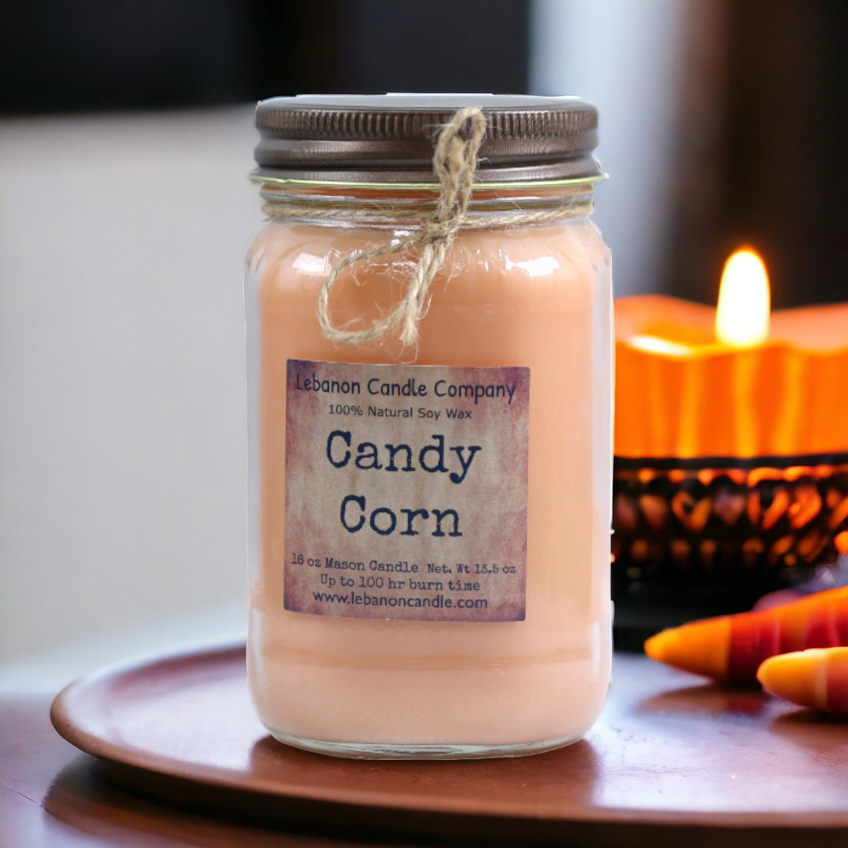 Peach jar candle with flame nearby, metal lid, Candy Corn label