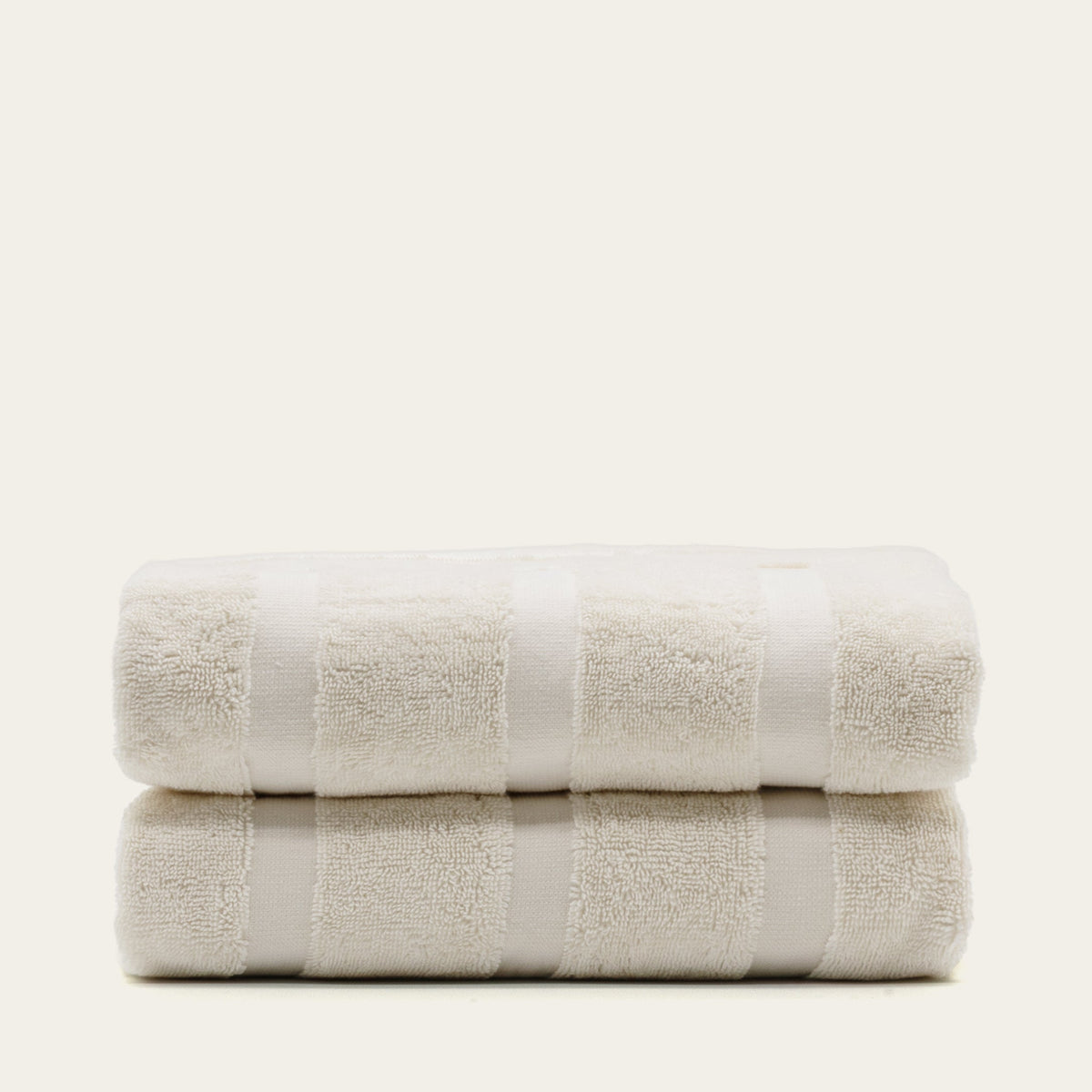 Two rolled off-white cotton towels with textured stripe bands and plush loops