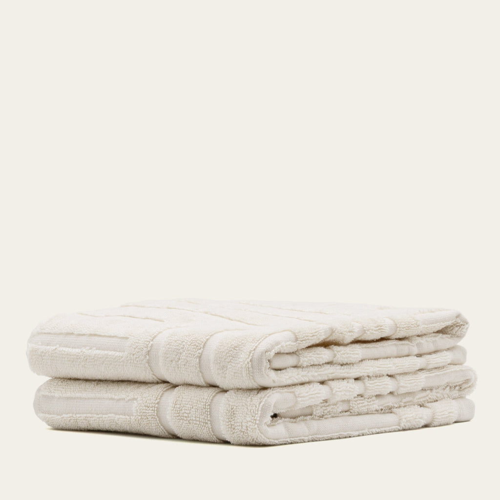 Ecru cotton towels stacked with textured stripes and stitched edge