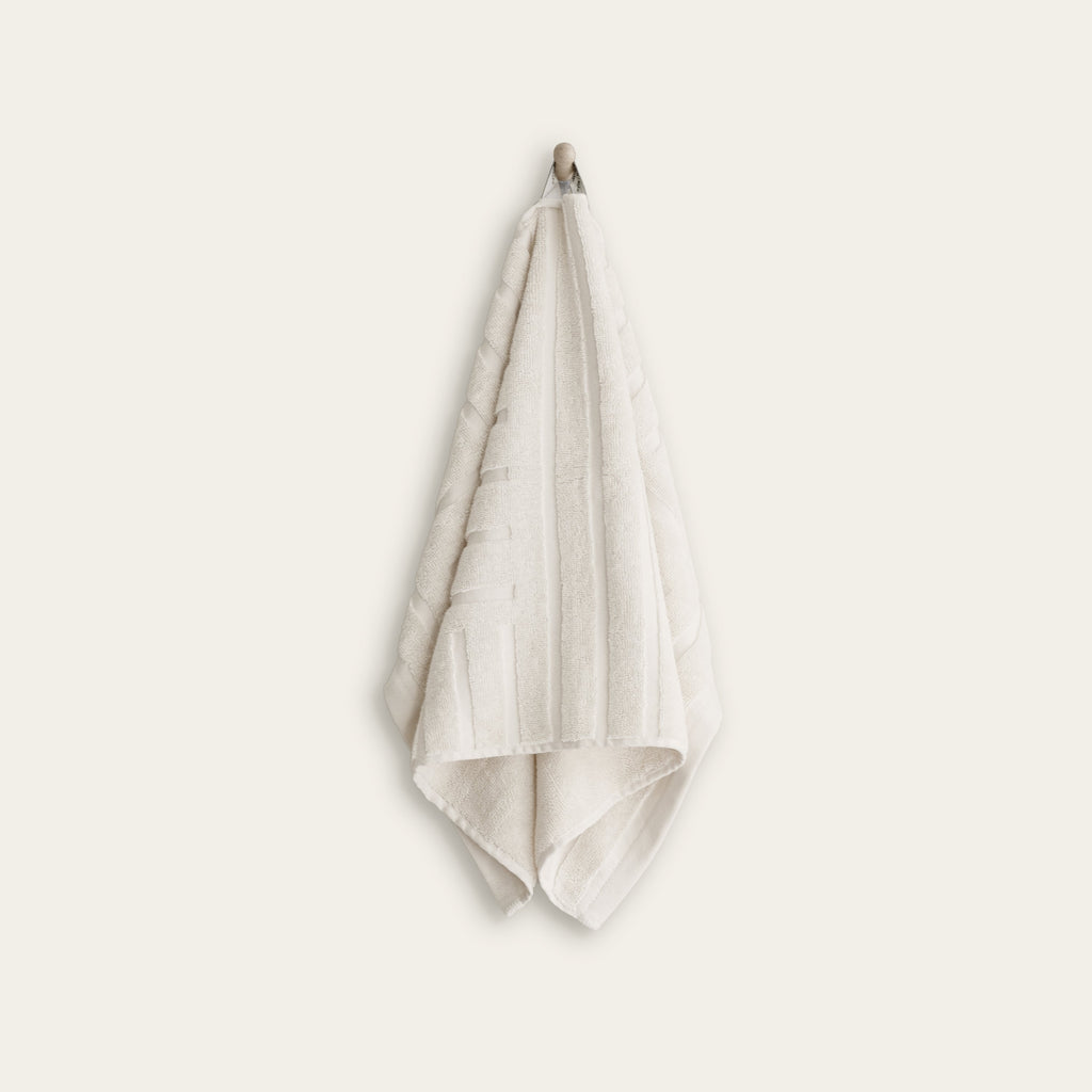 Ecru hand towel folded and draped over hook, textured terry weave