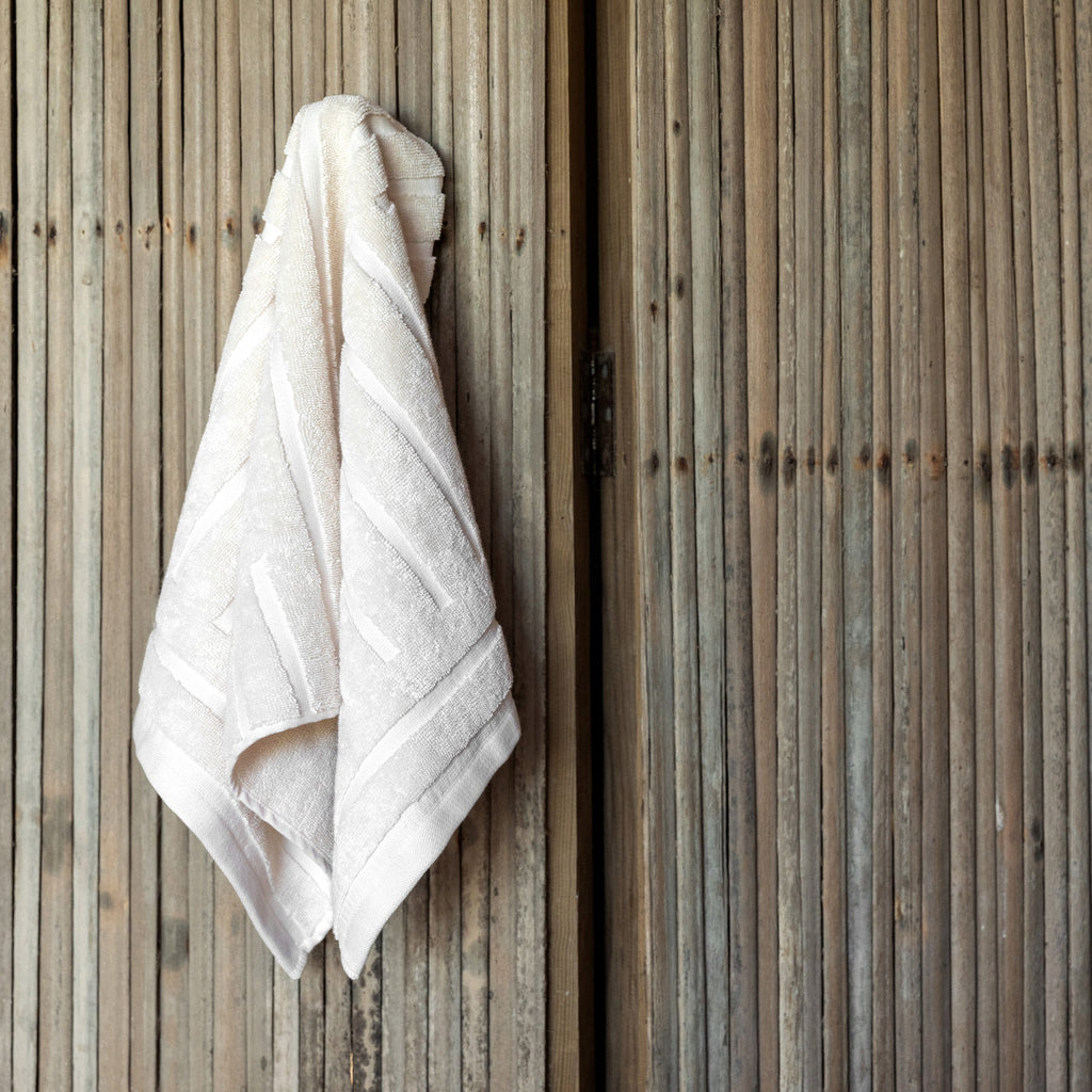 Ecru cotton towel hanging from wooden fence, terry texture with woven border