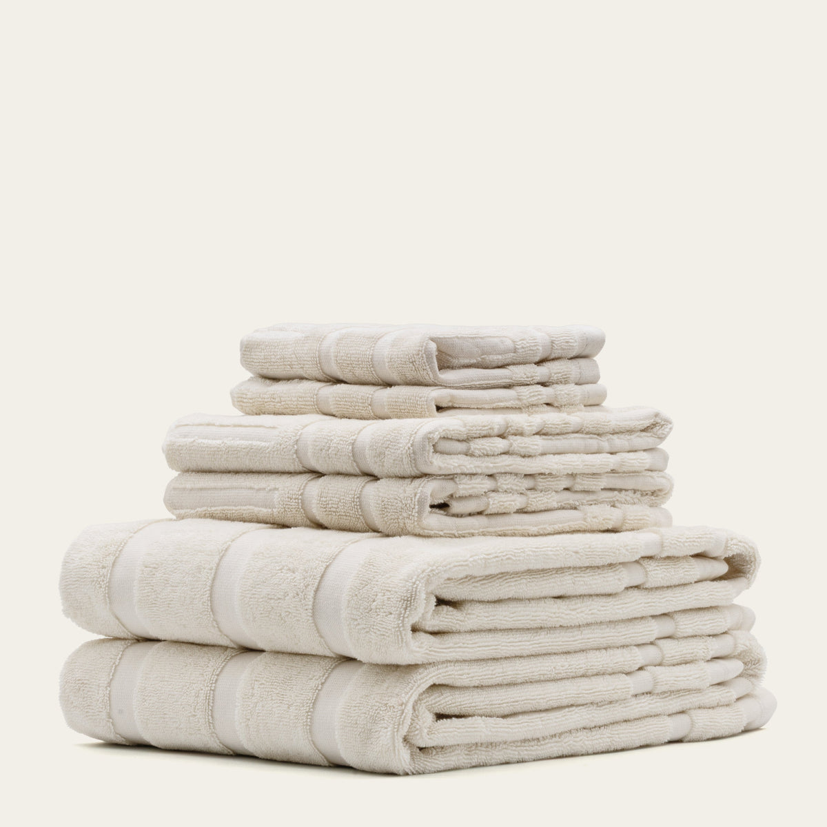 Stack of light beige cotton bath towels with striped band detailing