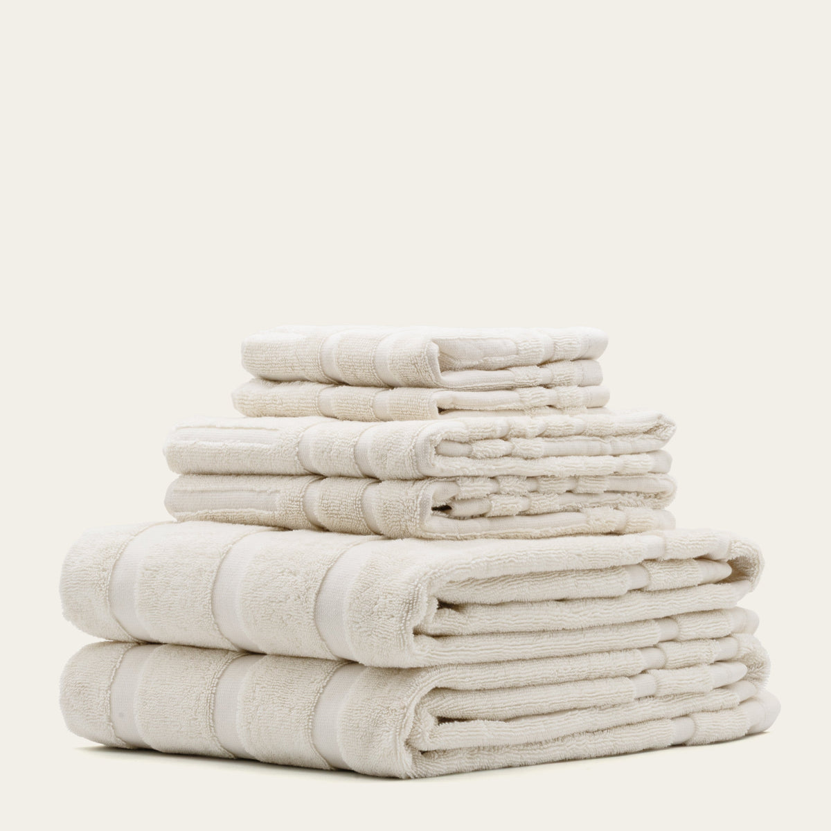 Stack of off-white cotton towels with banded stripes and plush terry texture