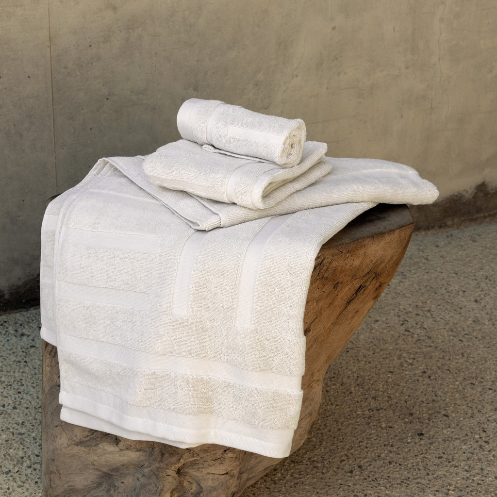 Folded white and ecru cotton towels stacked on a wooden surface with stripe bands.